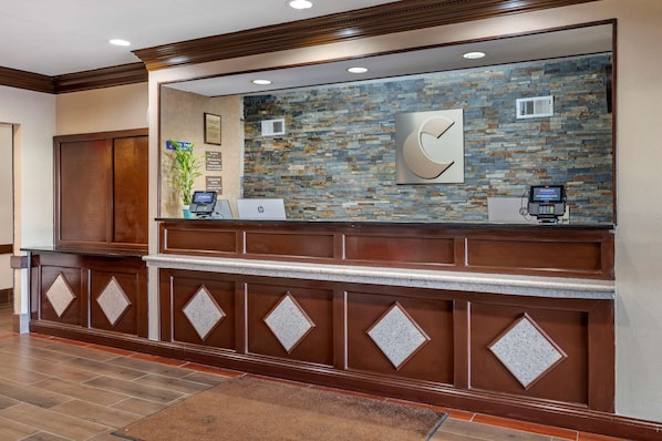 A reception area with a stone wall, a wooden reception desk, and a digital kiosk. - Comfort Inn & Suites Cincinnati Uptown Clifton (Cincinnati)