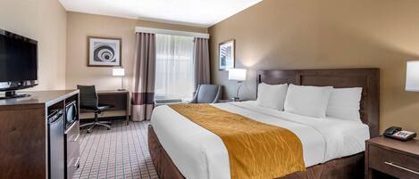 A hotel room with a large bed, a desk with a chair, a TV, and a telephone.