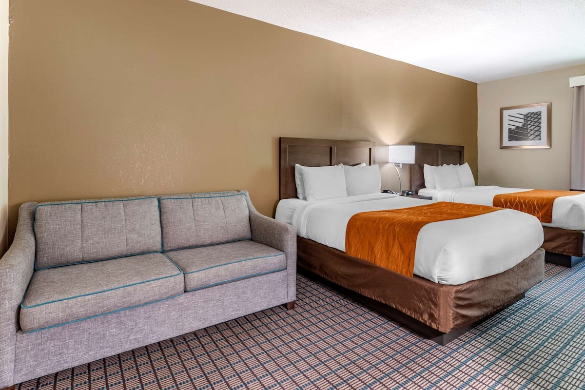 A hotel room with a sofa, two beds, a patterned carpet, and a framed picture on the wall.