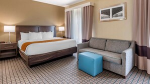 A hotel room with a bed, two bedside lamps, a sofa, a blue ottoman, and a window with curtains. - Comfort Inn & Suites Cincinnati Uptown Clifton (Cincinnati)