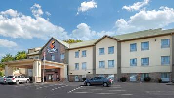Un hotel Comfort Inn & Suites con aparcamiento, una entrada cubierta y un cielo azul despejado con nubes.