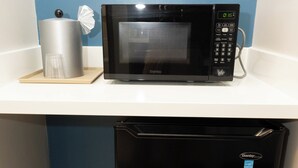 A compact kitchen with a black microwave on a white countertop, a silver container, and a black refrigerator.