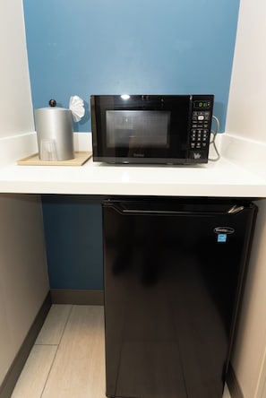 A compact kitchen with a black microwave on a white countertop, a silver container, and a black refrigerator.