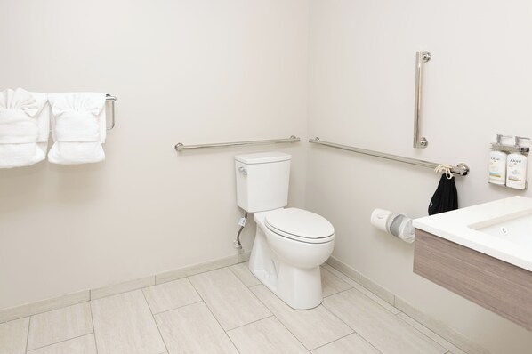 A modern bathroom with a toilet, handrails, a towel rack, and a sink.