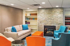 A modern lounge area with a beige sofa, blue and orange chairs, a fireplace, and bookshelves. - Holiday Inn Express Hotel & Suites Mt. Holly by IHG (Mount Holly)