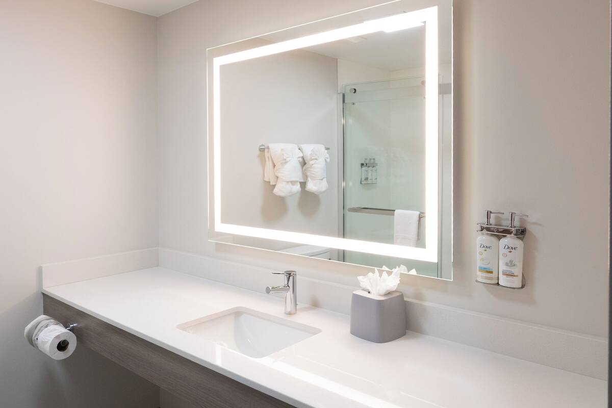 A modern bathroom with a large mirror, a sink, and a glass shower enclosure.