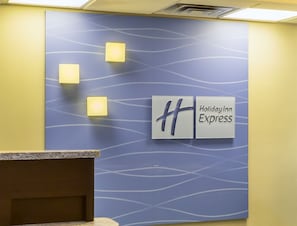 A Holiday Inn Express reception desk with a blue patterned wall and three illuminated square signs.