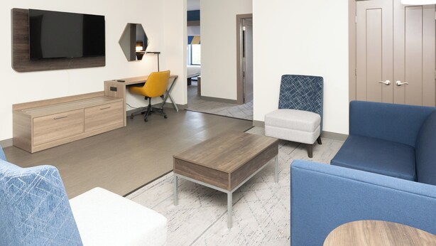 A modern living room with a flat-screen TV, a wooden coffee table, a blue sofa, and a small ottoman.