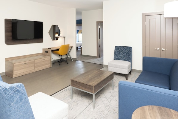 A modern living room with a flat-screen TV, a wooden coffee table, a blue sofa, and a small ottoman.