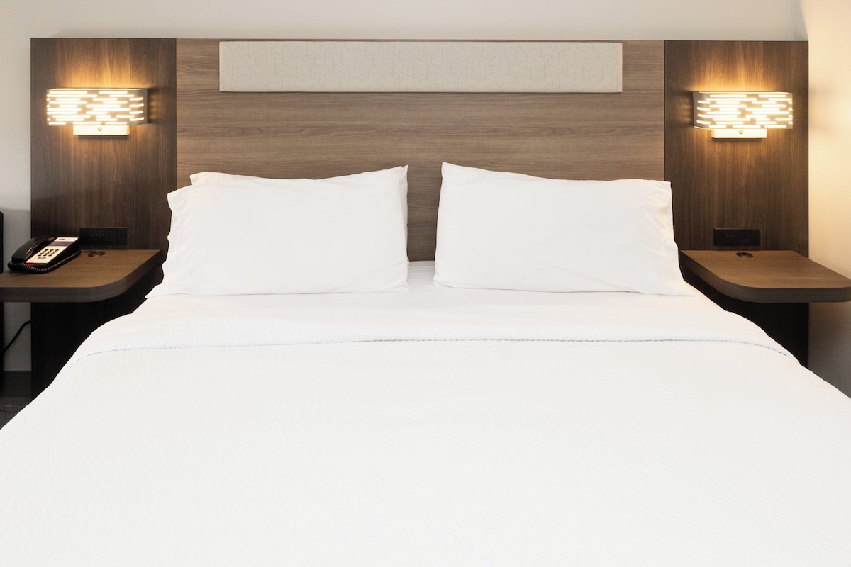 A hotel room with a large bed, two bedside tables, a nightstand, a wall-mounted light fixture, and a map on the wall.