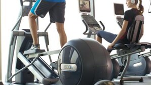 A gym with treadmills and stationary bikes, large windows, and exercise balls.