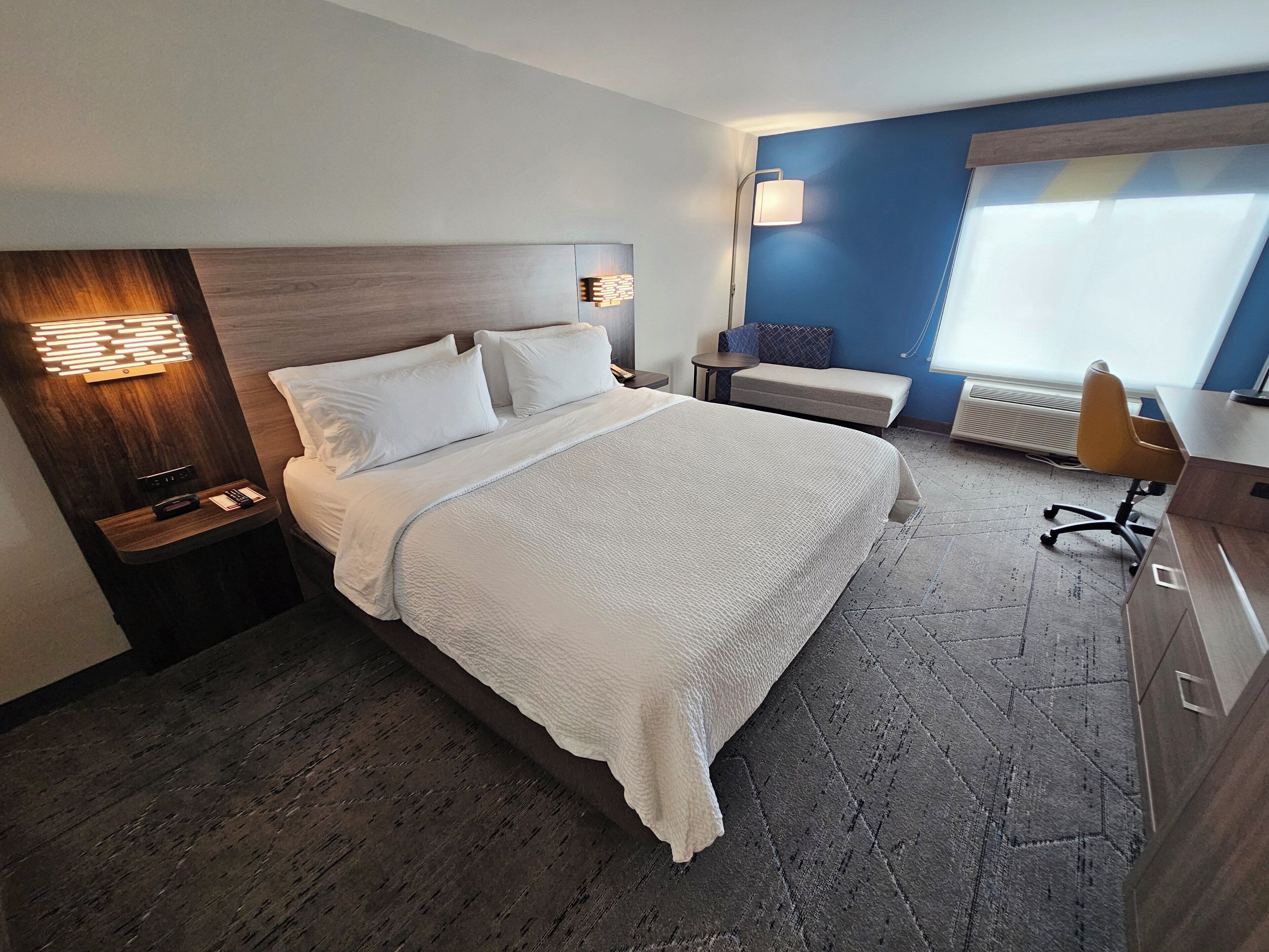 A hotel room with a large bed, bedside tables, a desk, a chair, and a window with blinds.