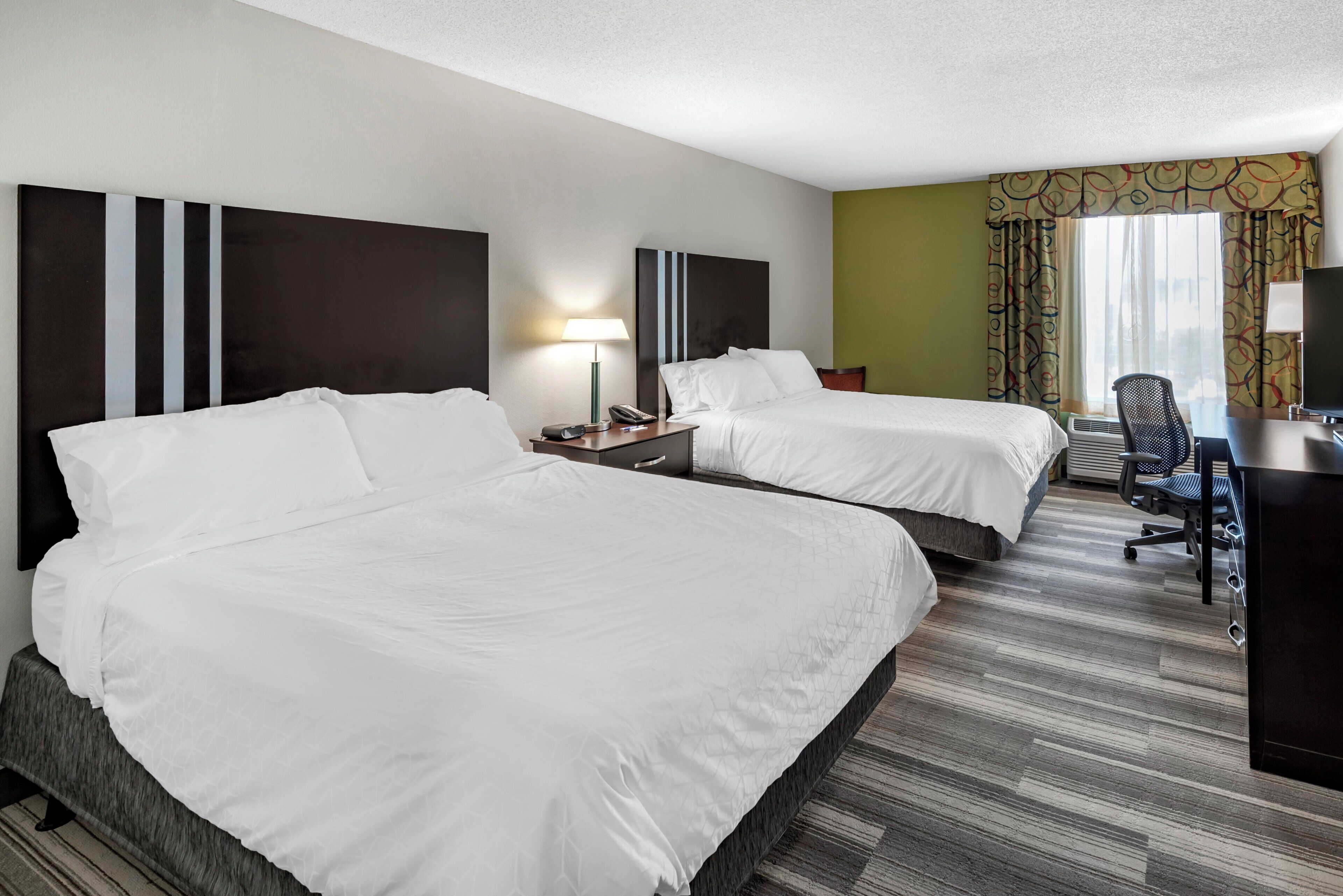Ein Hotelzimmer mit zwei Betten, einem Schreibtisch, einem Stuhl und einem Fernseher.
