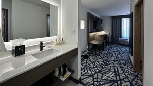 A modern hotel bathroom with a large mirror, a white sink, a vanity, and a shower area.