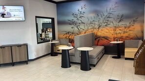 Un interior moderno con un sofá, dos mesas redondas, una estación de café y un televisor montado en la pared.