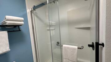 A glass-enclosed shower with a handheld showerhead, a towel rack with folded towels, and a toilet visible in a bathroom with blue walls.