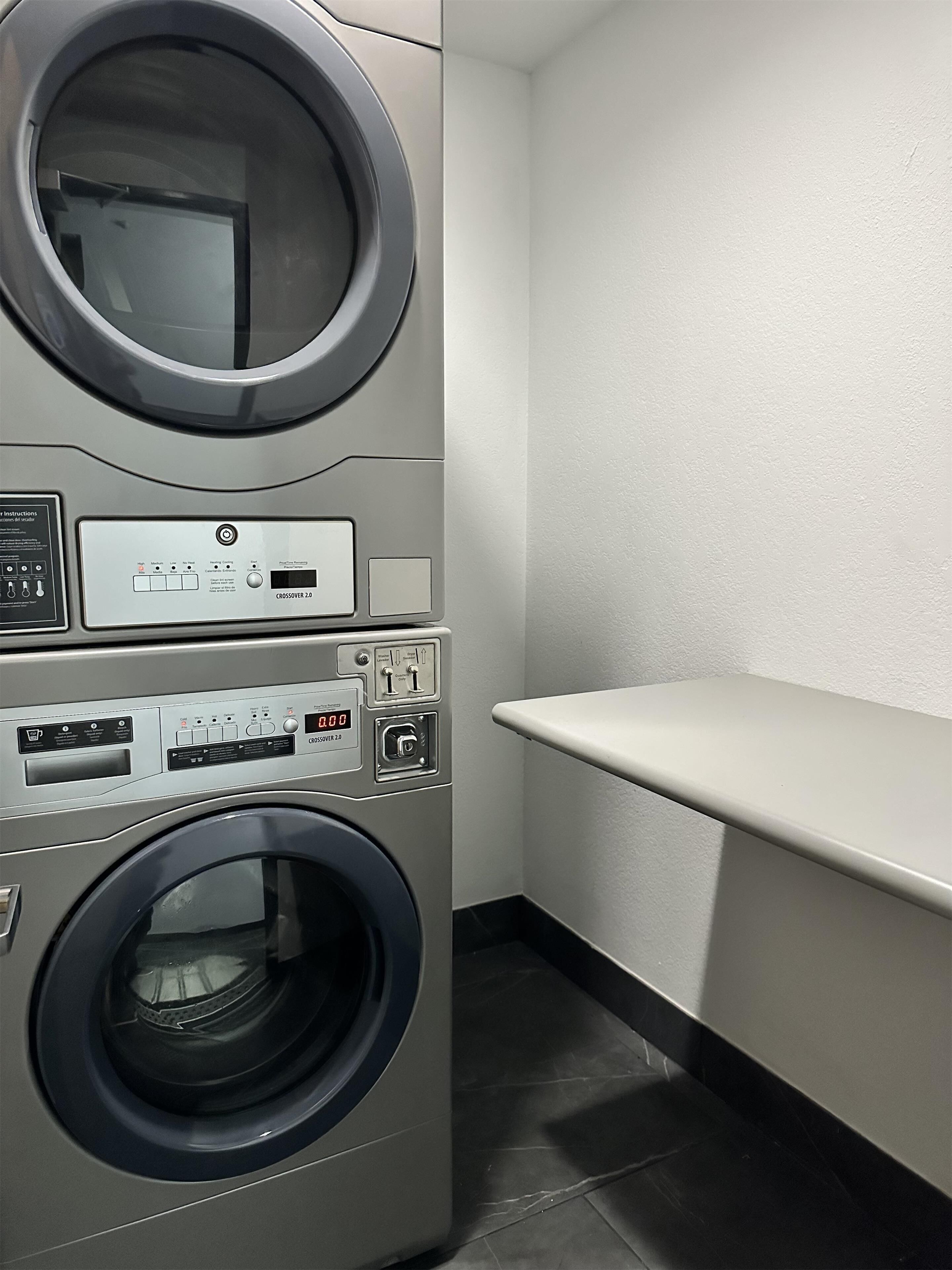 Een wasruimte met gestapelde wasmachines en drogers, bedieningspanelen en een wit schap.