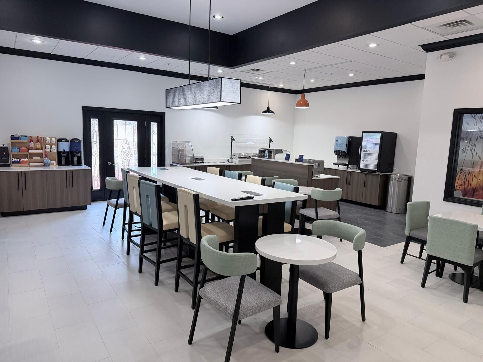 Un café moderne doté d’une grande table commune, de sièges individuels, d’une machine à café et d’un menu numérique.