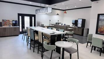 Un café moderne doté d’une grande table commune, de sièges individuels, d’une machine à café et d’un menu numérique.