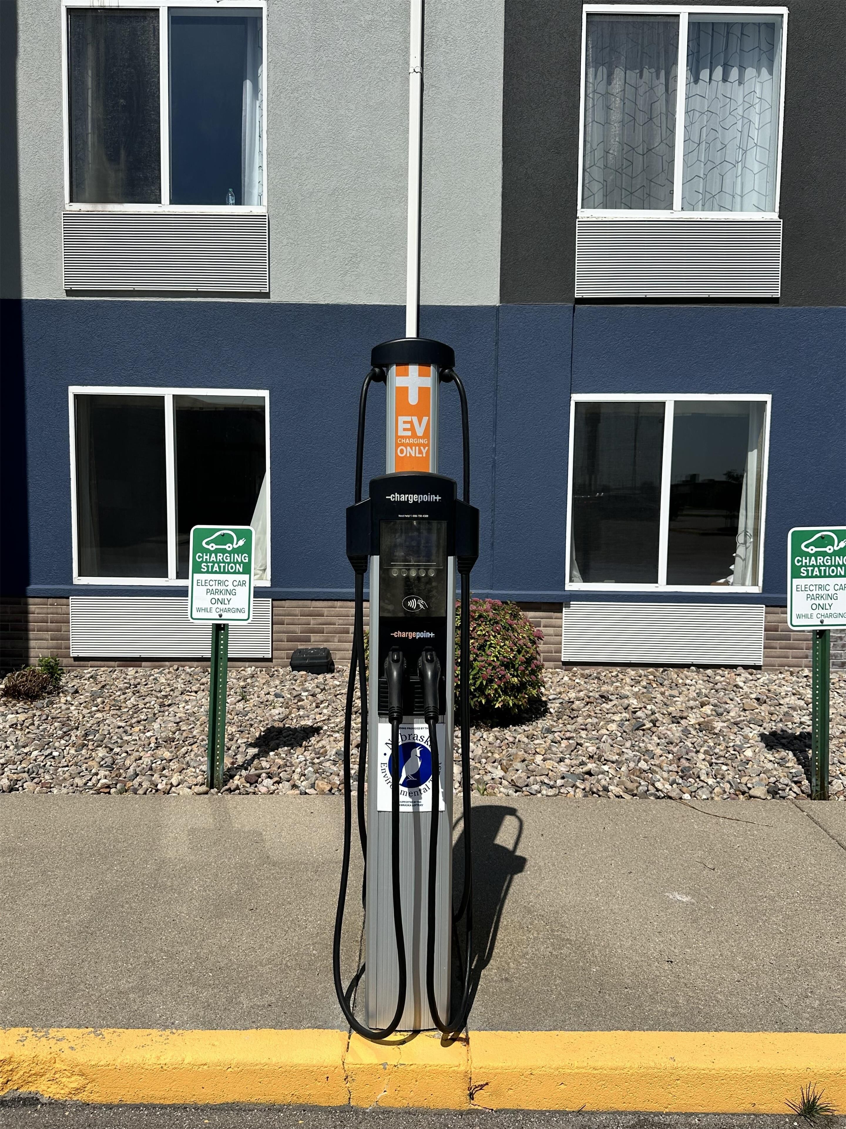 An electric vehicle charging station with a sign indicating it is for EV charging only, located in front of a building with windows and a brick wall.