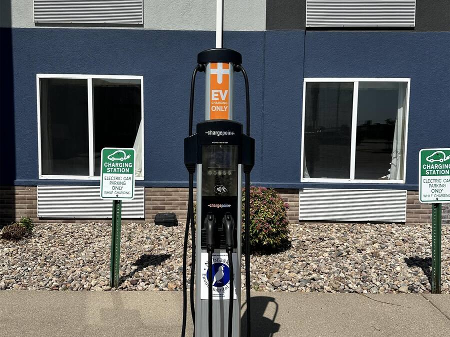 An electric vehicle charging station with a sign indicating it is for EV charging only, located in front of a building with windows and a brick wall.