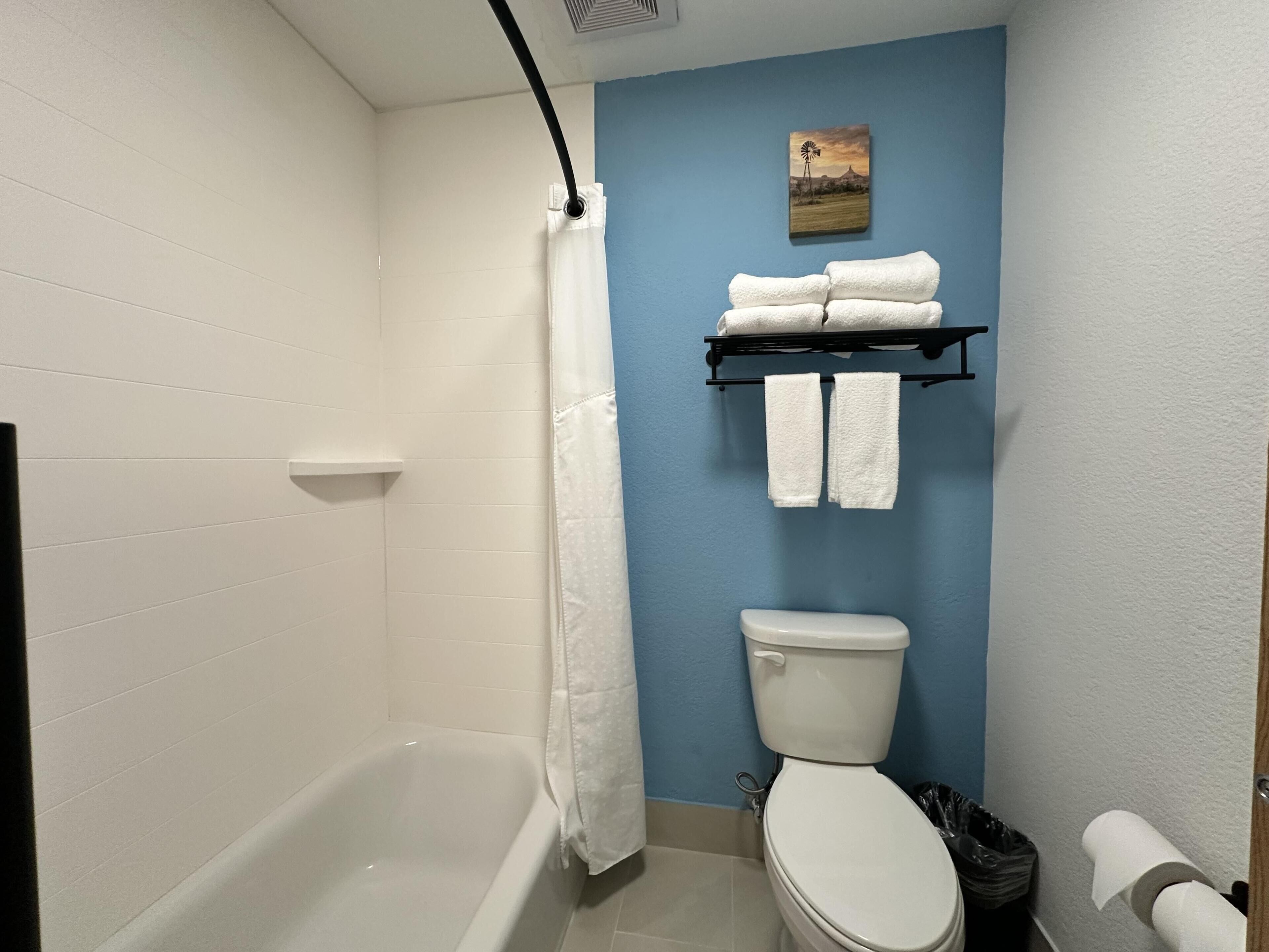 Un baño con bañera, inodoro y toallero con toallas.