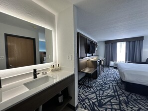 Une chambre d’hôtel avec un grand miroir, une porte en bois, un téléviseur à écran plat, un lit, un bureau et une moquette à motifs.