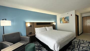 Una habitación de hotel con cama, escritorio, silla, lámpara, cuadro y puerta.