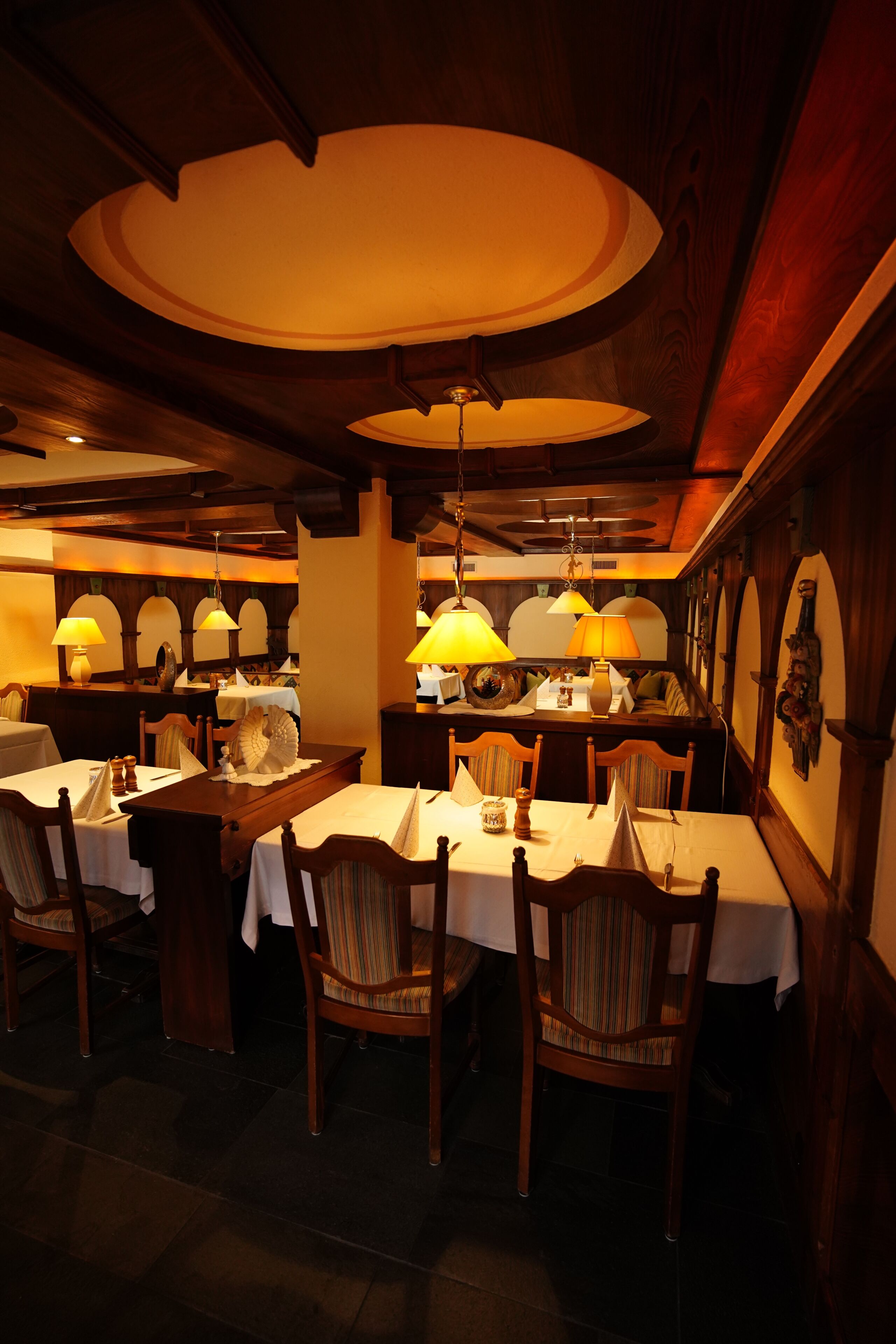 Ein Restaurantinnenraum mit Holztischen, Stühlen und hängenden Lampen.