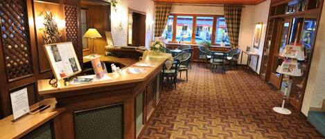 A hotel lobby with a reception desk, seating area, and a patterned carpet.
