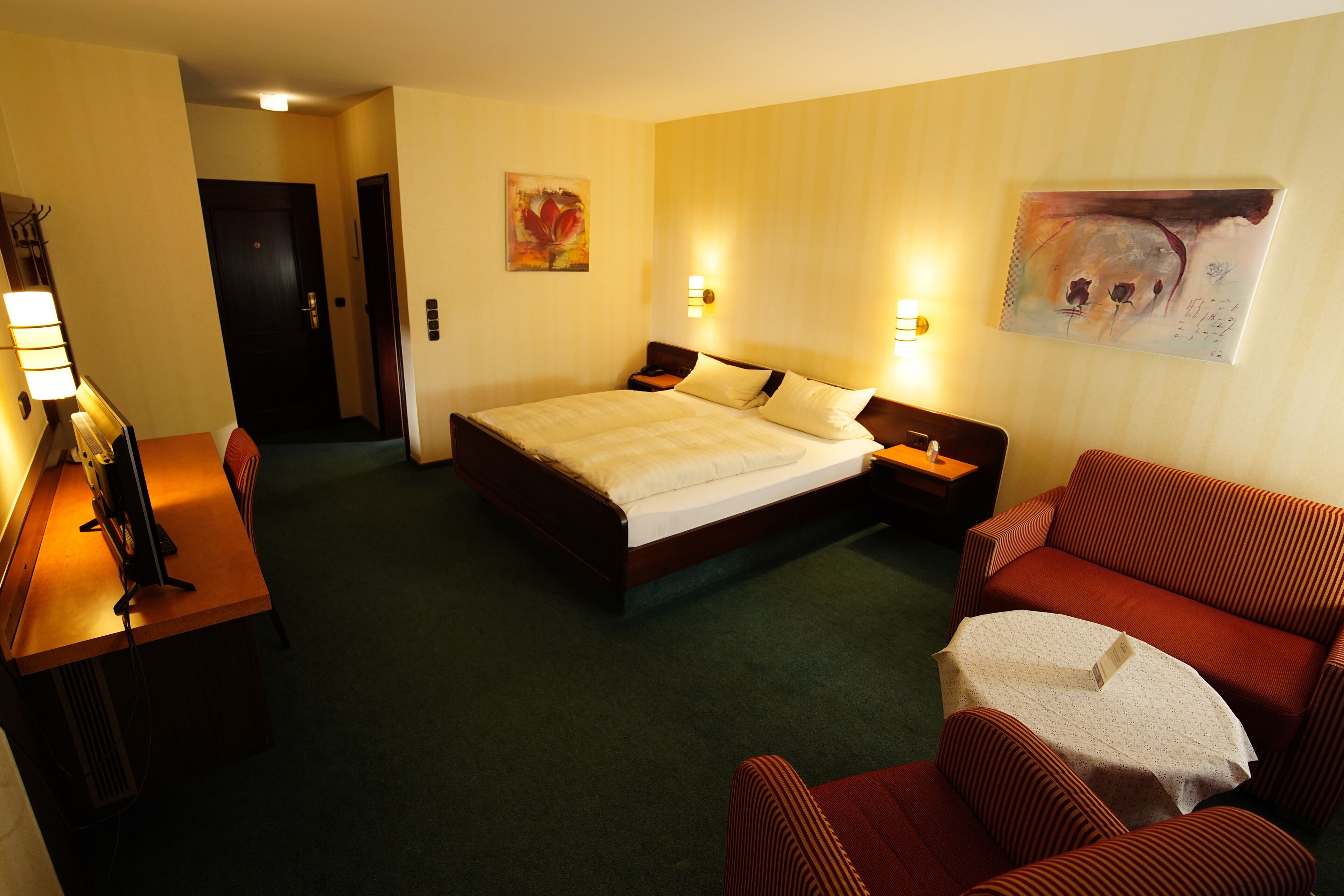 A hotel room with a bed, a desk with a computer, a sofa, and two wall-mounted lamps.