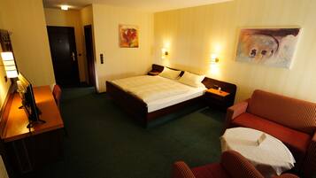 A hotel room with a bed, a desk with a computer, a sofa, and two wall-mounted lamps.