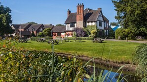 A traditional Tudor-style building with a large lawn and picnic tables. - The Moat House (Stafford)
