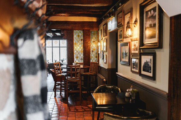 A cozy interior with wooden furniture, a tiled floor, and a wall adorned with framed pictures. - The Moat House (Stafford)
