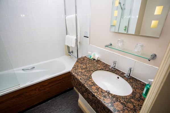 A bathroom with a white bathtub, a granite sink, and a glass shelf above the sink. - The Moat House (Stafford)