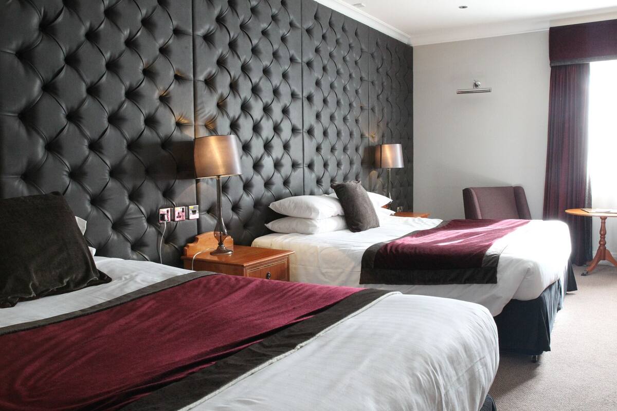 A hotel room with two beds, a tufted headboard, bedside lamps, and a small round table.