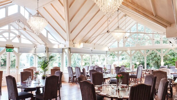 A spacious dining area with high ceilings, chandeliers, and large windows offering a view of the outdoors. - The Moat House (Stafford)