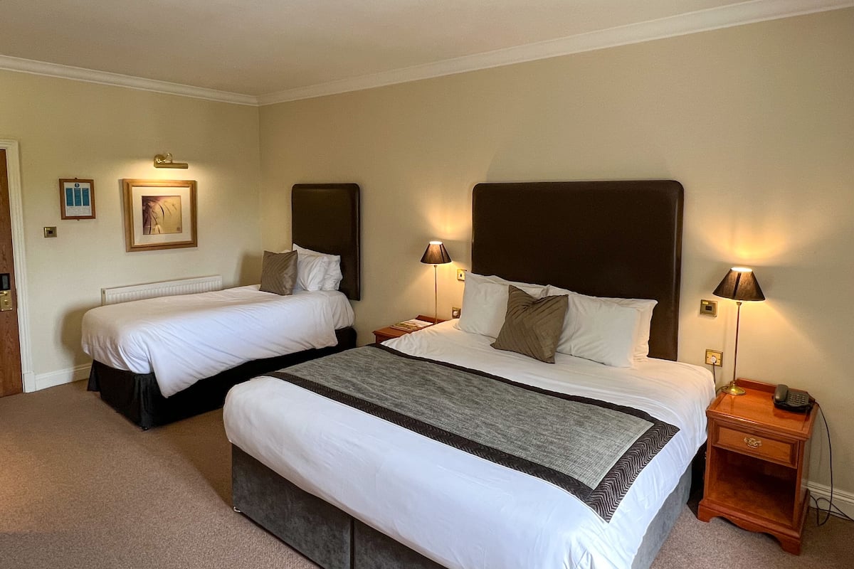 A hotel room with two beds, each with a headboard, bedside lamps, and a small wooden nightstand with a phone.