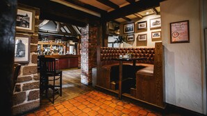 A cozy bar area with a brick wall, wooden ceiling beams, and a seating area with cushioned booths. - The Moat House (Stafford)