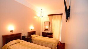 A hotel room with two beds, a mirror, a nightstand, a lamp, and a TV mounted on the wall. - Balasca Hotel (Athens)