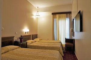 A hotel room with three beds, a desk, a chair, and a television.
