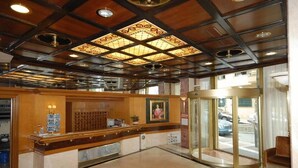 A hotel lobby with a reception desk, a glass door entrance, and a seating area. - Balasca Hotel (Athens)