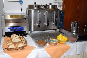 Egy konyhasarok, amelyben található egy kenyérsütő gép, egy nagy, rozsdamentes acélból készült tartály, amelyen több csaptelep is van, valamint egy büféasztal, amin kenyér, különböző feltétek és egy kosár található.