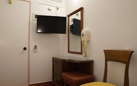 A room with a bed, a wooden chair, a vanity with a mirror, and a television mounted on the wall.