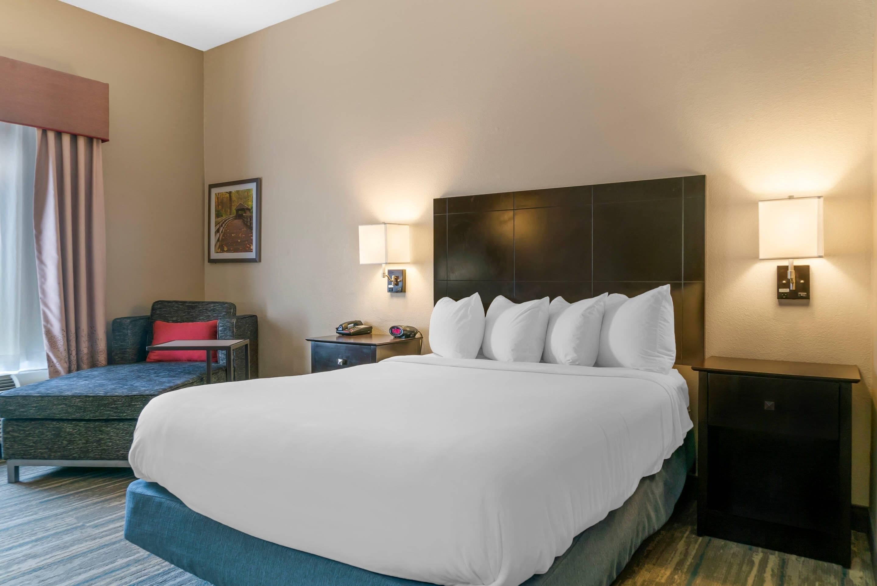 Habitación de hotel con una cama grande, un escritorio, una silla y una mesita de noche con lámparas.