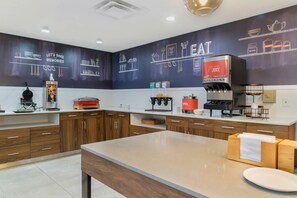 A modern kitchen with wooden cabinets, a countertop with a waffle maker, a coffee machine, and a juice dispenser. - Comfort Inn & Suites Toledo North (Toledo)