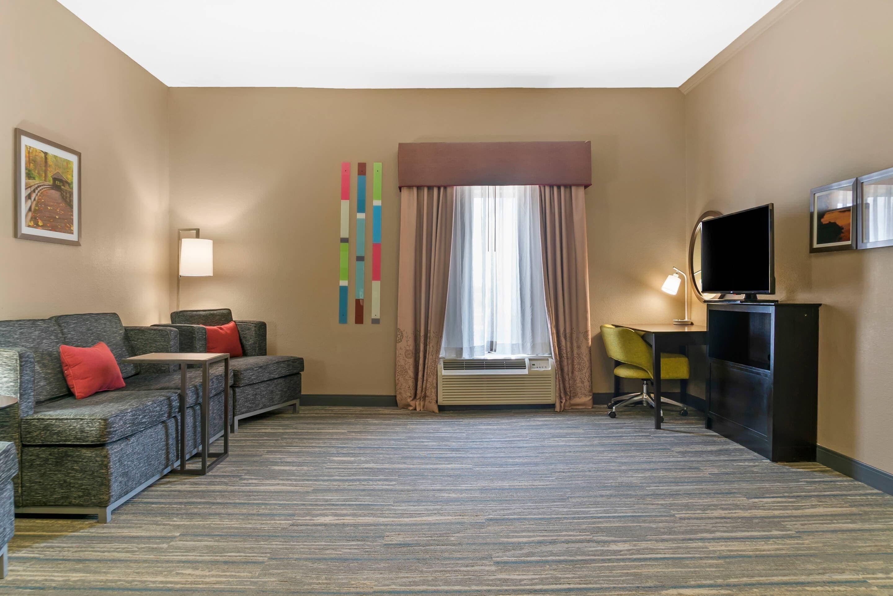 A hotel room with a sofa, a desk, a television, and a window with curtains.