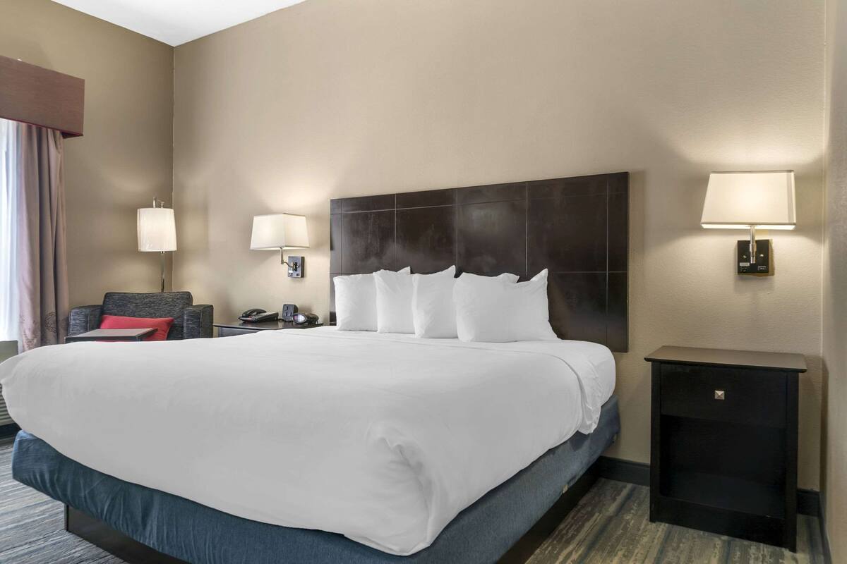 Una habitación de hotel con una cama grande, dos lámparas de noche, una mesita de noche y una silla.