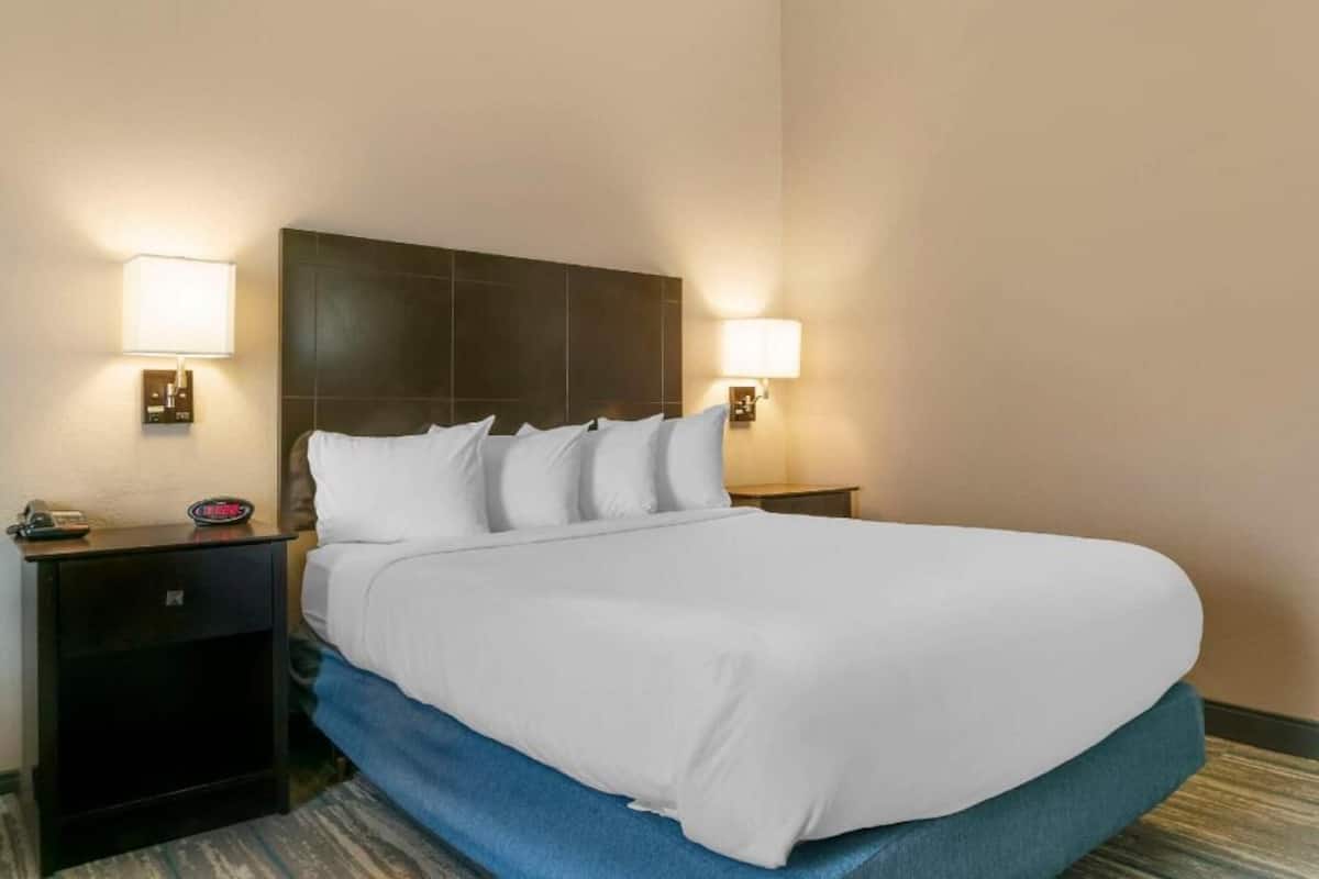 Una habitación de hotel con una cama grande, dos mesitas de noche y lámparas de pared.