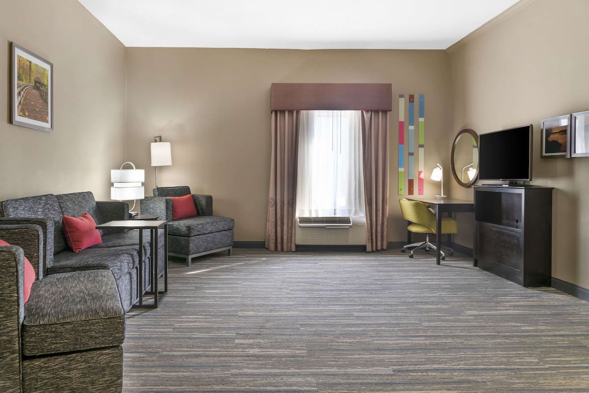 Habitación de hotel con sofá, sillón, escritorio, silla, televisión y espejo.